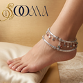 Silver anklets with star charms on a foot, placed on a beige cushion with 'Sooma' brand logo.