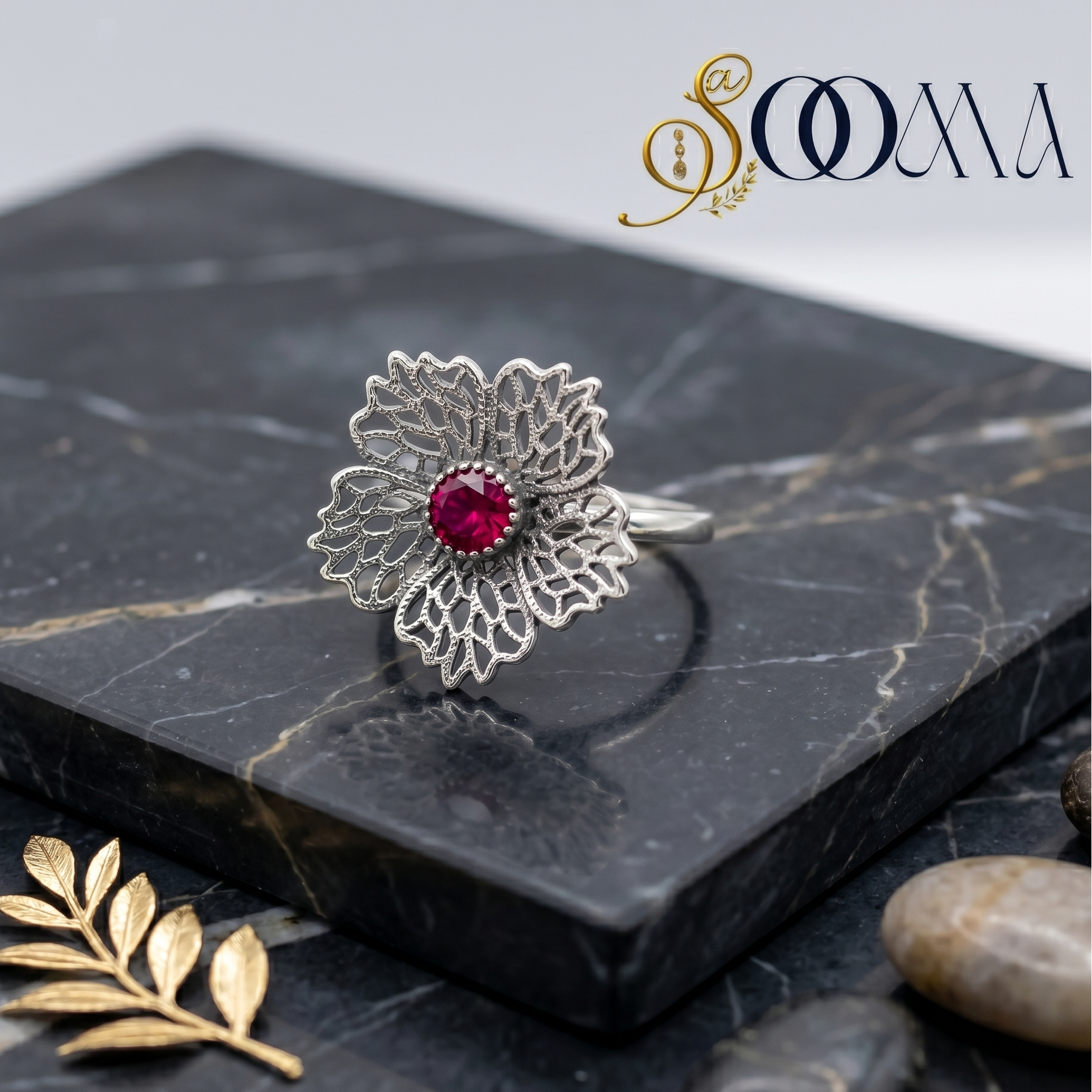 Close up of Sooma brand intricate silver filigree flower toe ring featuring a brilliant cut ruby red center stone on a black marble background