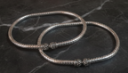 Two silver ankle bracelets with decorative elements on a dark marble surface