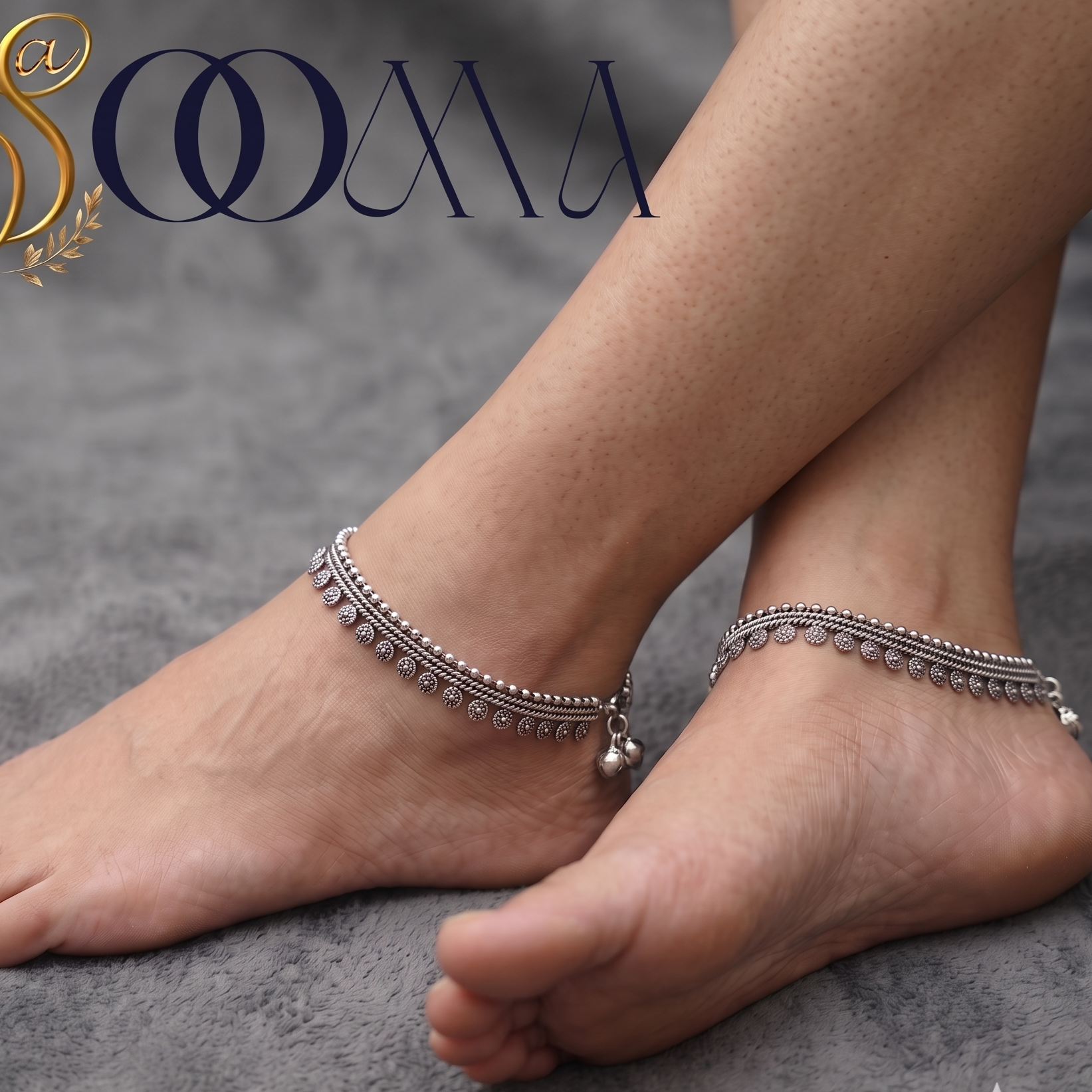 A pair of silver-toned ankle bracelets with rhinestone-like detailing and dangling bead charms, shown worn on bare feet against a gray textured background. The brand name 'SOOMA' appears in the upper left.