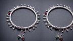 Two silver ankle kadas with star and gemstone charms on a dark background