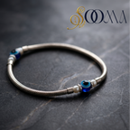 Silver bracelet with blue and white beads on a dark textured surface, featuring the brand 'Sooma'.