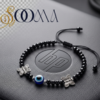 A black beaded anklet with silver butterfly charms and a blue evil eye bead, displayed on a dark textured surface with an HP logo in the background. The brand name 'SOOMA' is visible in the top left corner.