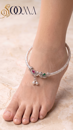 Top-down perspective of woman's foot wearing rigid silver elephant payal with green and ruby stones
