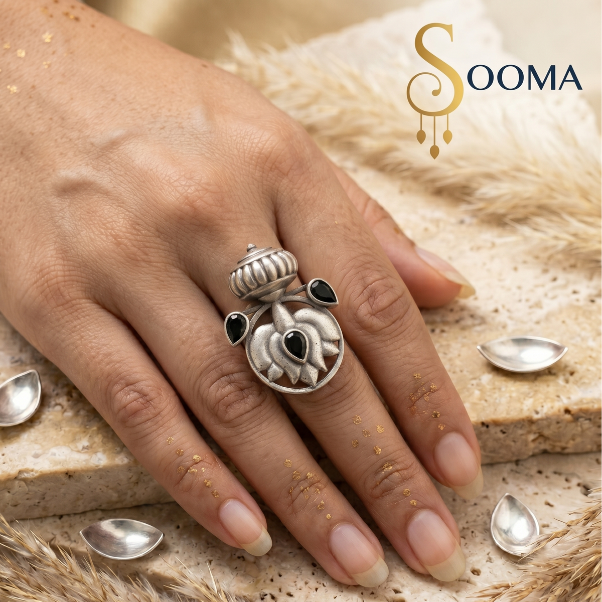 A silver-toned ring with a detailed floral and crown-like design, worn on a hand. The ring features black teardrop-shaped stones and a central black oval stone.
