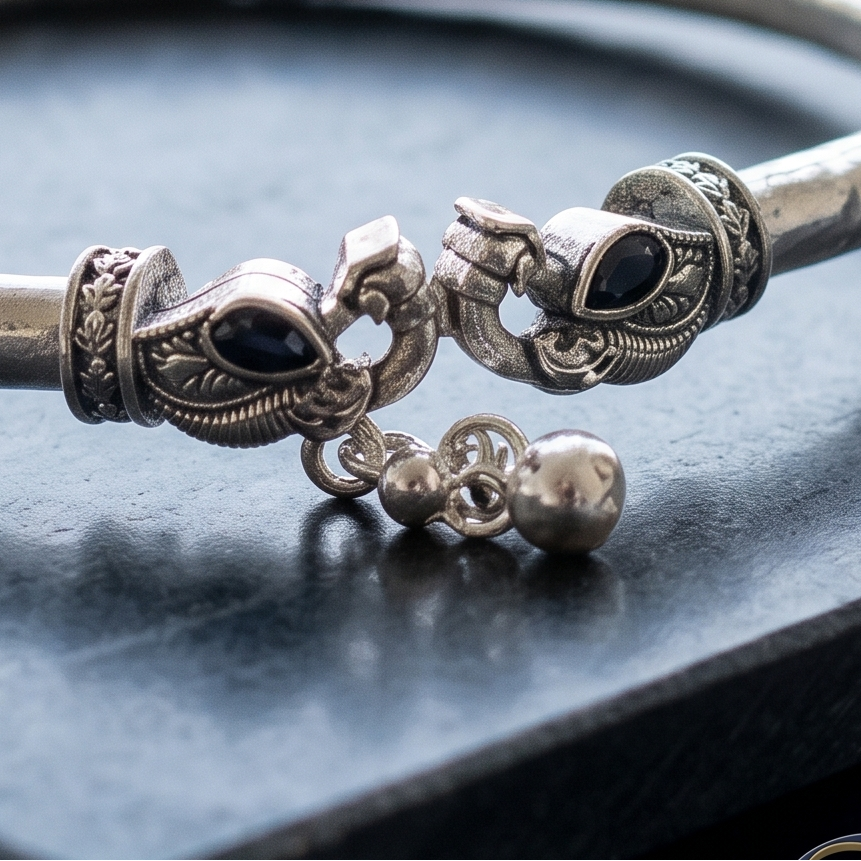 Handcrafted rigid silver kada anklet featuring dual elephant heads heads with stone studs displayed on dark slate