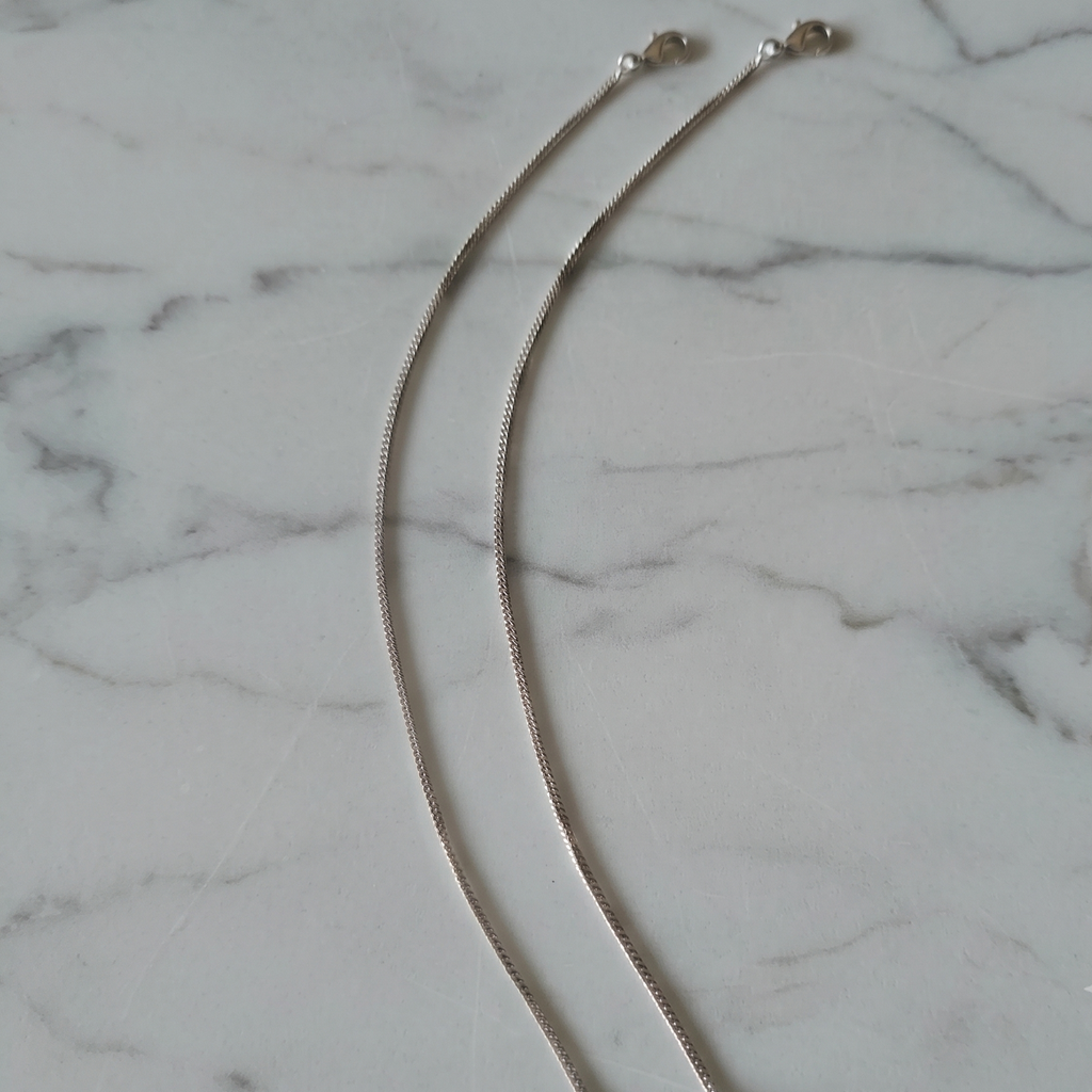Two silver chain anklets with lobster clasps, laid out on a white marble surface.