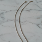 Two silver chain anklets with lobster clasps, laid out on a white marble surface.