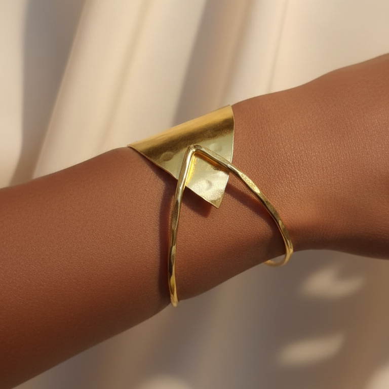 Gold cuff bracelet on a person's wrist with a neutral background
