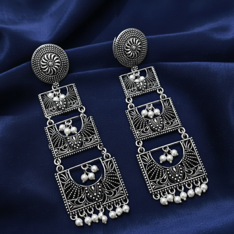 Close-up of handcrafted oxidised earrings with a long, layered design on blue background .