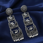 Close-up of handcrafted oxidised earrings with a long, layered design on blue background .