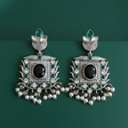 Traditional ornate silver earrings with black and green stones on a dark green background