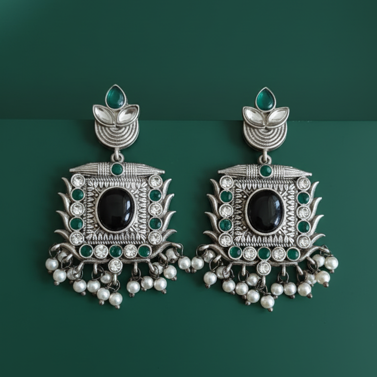Traditional ornate silver earrings with black and green stones on a dark green background