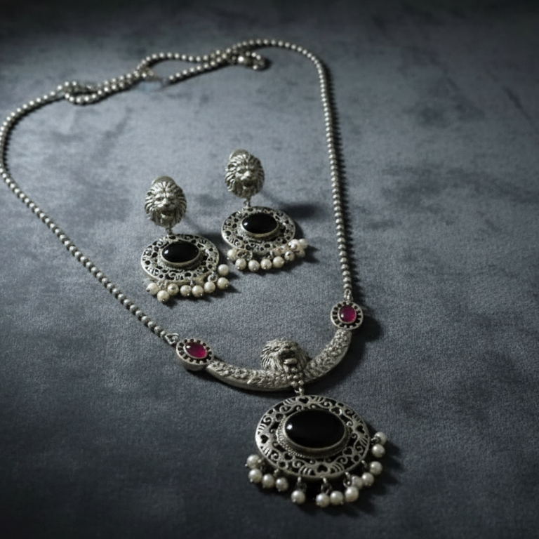 Oxidised silver necklace and earrings set on a dark textured surface