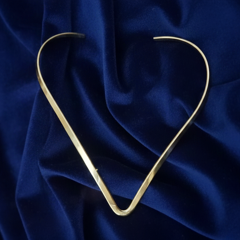 Elegant Modern Gold Hasli Necklace, minimalist design for versatile wear, against blue background .