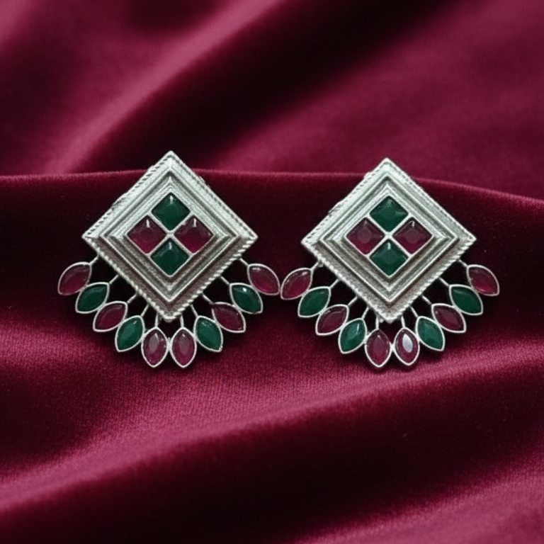 Pair of Oxidized Silver Peacock Stud Earrings with Green and Red Stones on a maroon fabric background