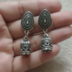 Oxidised silver earrings held between fingers on a neutral background