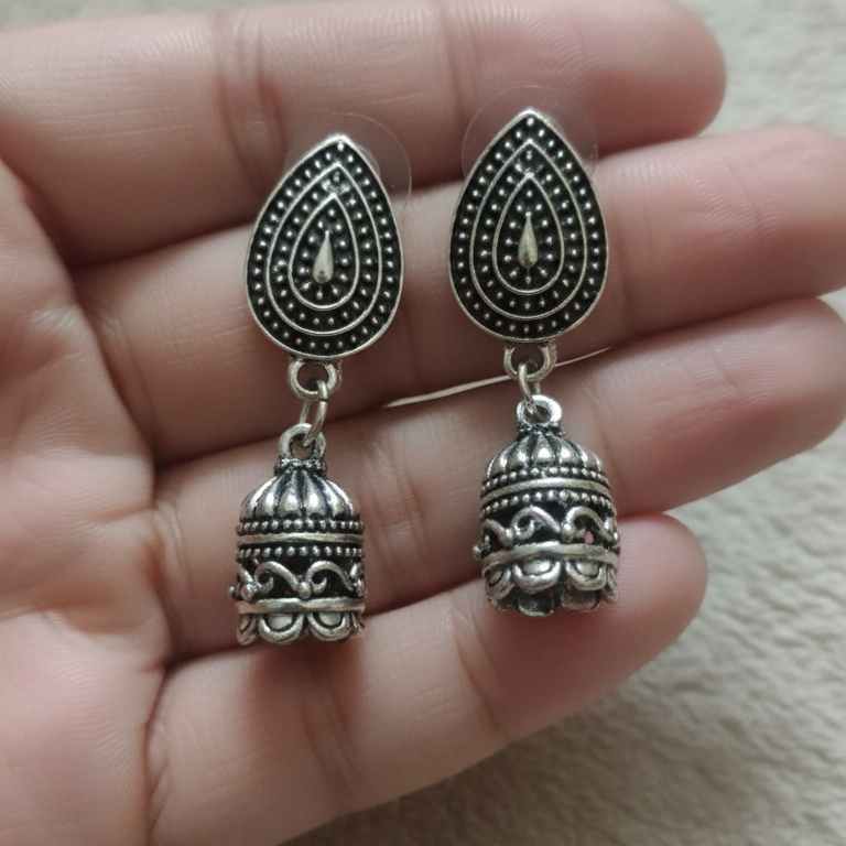 Oxidised silver earrings held between fingers on a neutral background