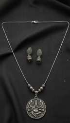 Silver necklace with pendant and matching earrings on a black fabric background