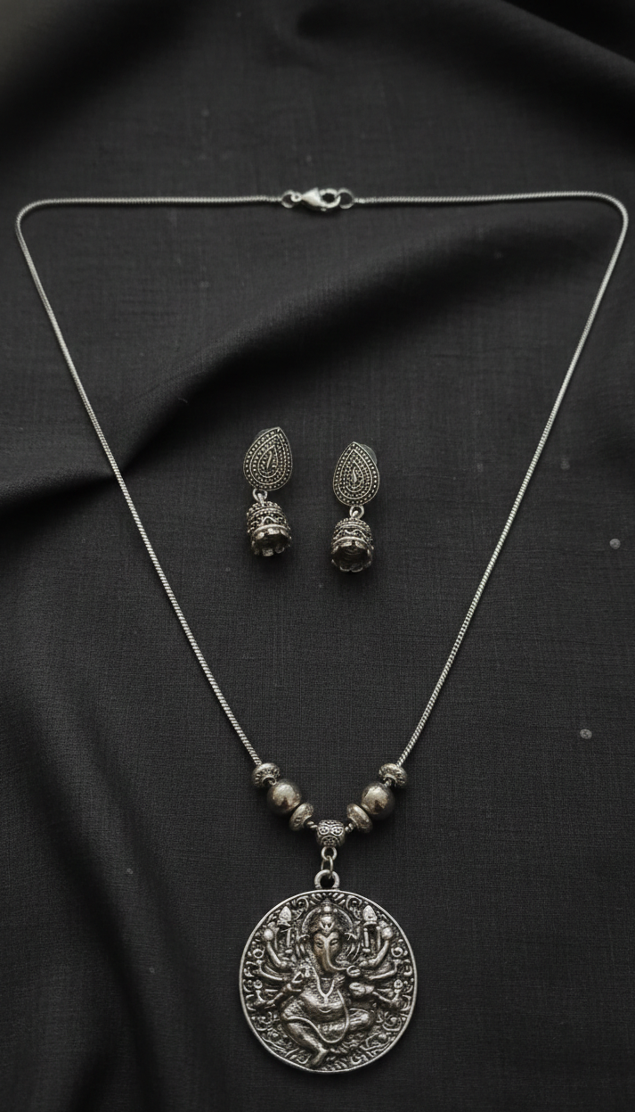 Silver necklace with pendant and matching earrings on a black fabric background