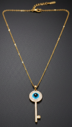 Gold necklace with a key-shaped pendant featuring an evil eye design on a dark background