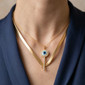 Minimalist gold hasli with evil eye pendant stack for professional women worn by a person in a blue outfit.