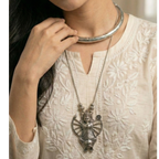 Woman wearing a stack of silver hasli with a detailed durga pendant on a neutral background