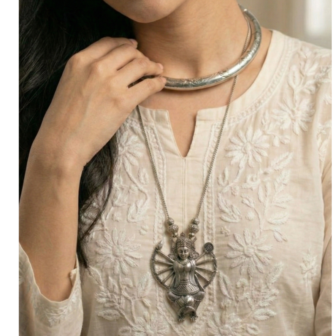Woman wearing a stack of silver hasli with a detailed durga pendant on a neutral background