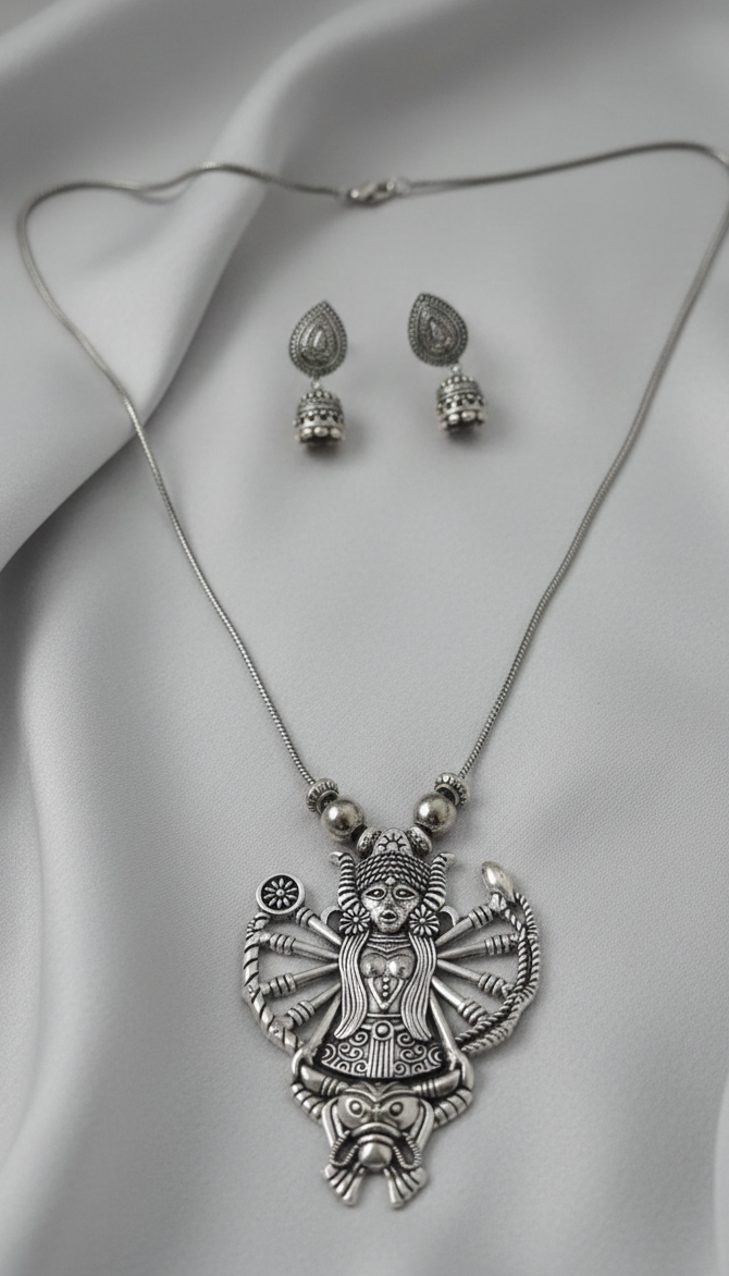 Silver Durga necklace and earrings on a gray fabric background