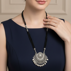 Woman wearing a long mangalsutra necklace with a decorative pendant against a neutral background