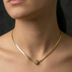 Gold necklace with a small stud pendant on a person's neck against a dark background
