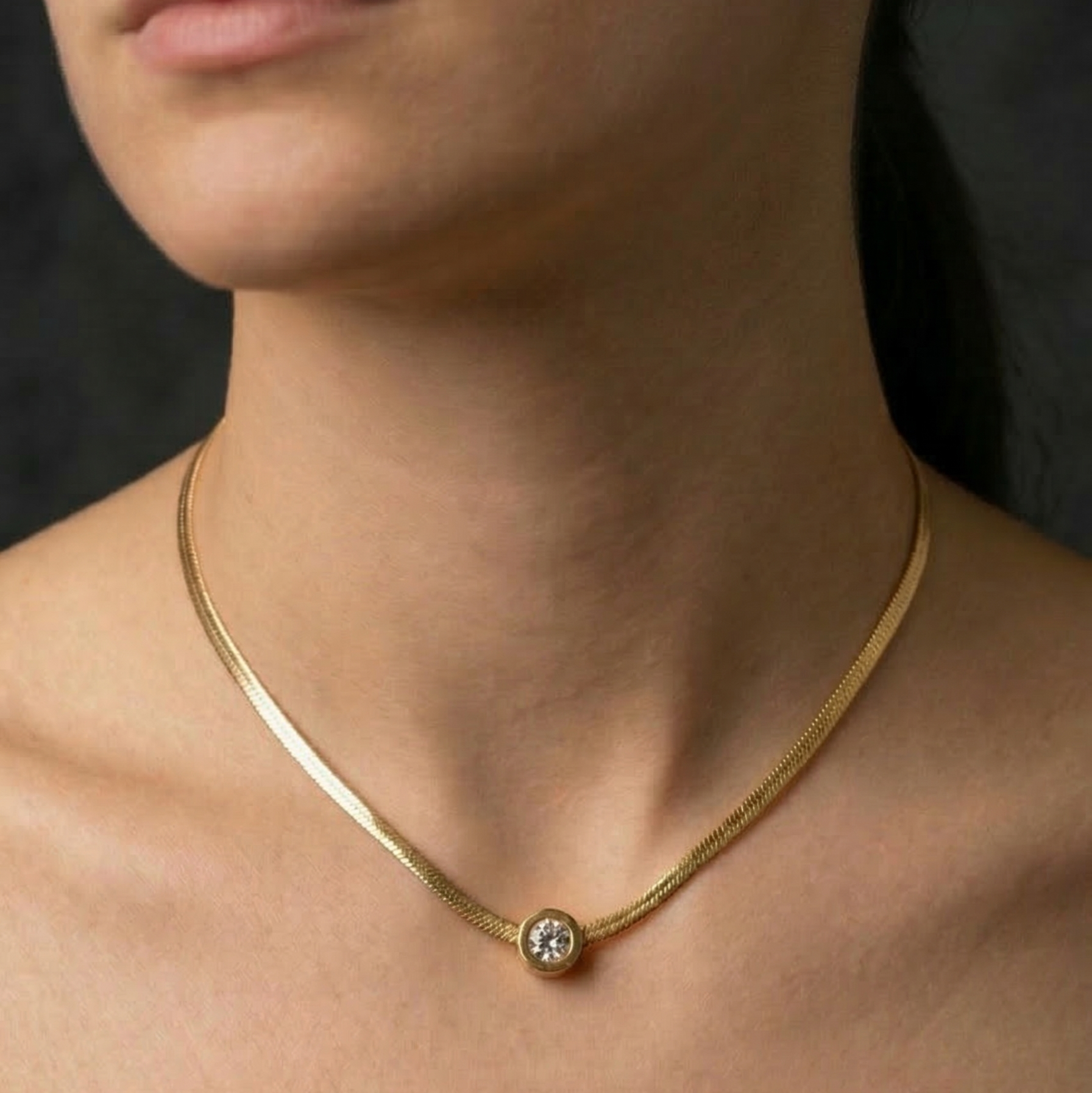 Gold necklace with a small stud pendant on a person's neck against a dark background