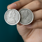Two silver coins earrings held in a hand against a dark background