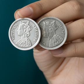 Two silver coins earrings held in a hand against a dark background