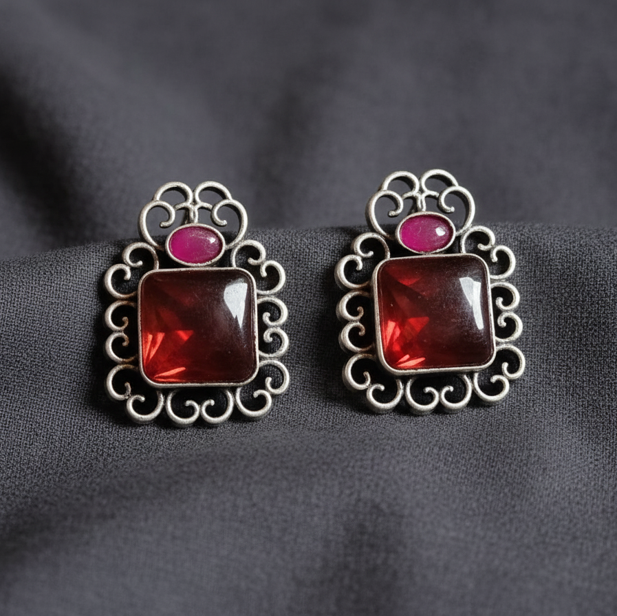 Red & Pink Oxidised stone stud earrings on a Grey background, close-up.