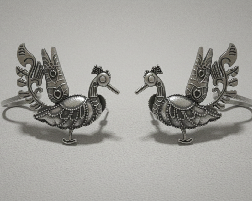 Pair of silver peacock-shaped earcuffs on a light gray background
