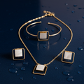 Gold jewelry set (necklace, earrings & bracelet )with square pendants on a dark blue surface