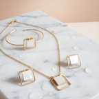 Gold pendant ,bracelet & earrings with square stones on a marble surface
