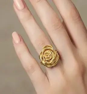 Gold rose-shaped ring on a hand against a neutral background