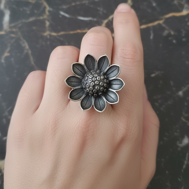 Hand wearing a silver flower-shaped ring on a dark marble surface