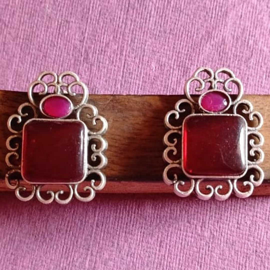 Red & Pink Oxidised stone stud earrings on a textured background, close-up.