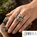 Silver ring with intricate design on a hand, brand logo visible