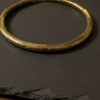 Rust gold traditional hasli necklace,  versatile statement piece on a claystone background.