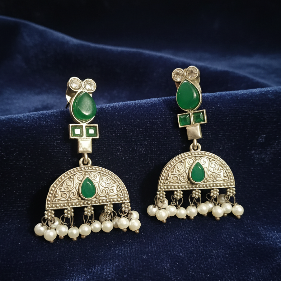 Close-up of Green Kundan drop earrings showcasing intricate stone settings. on a blue fabric background
