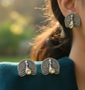 Silver peacock feather earrings worn by a person 