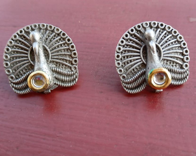Oxidised silver peacock stud earrings on a colored surface