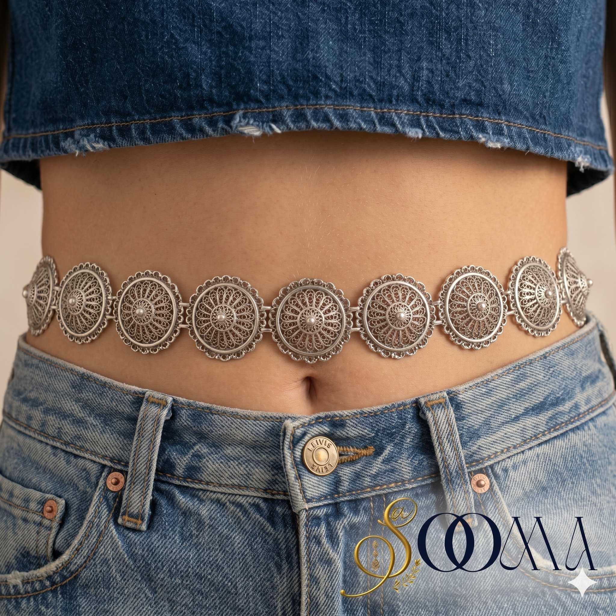 Person wearing a decorative silver belt with denim jeans, featuring the brand 'Sooma'.