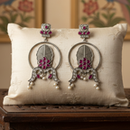 Pair of silver earrings with red gemstones on a white pillow with a decorative background
