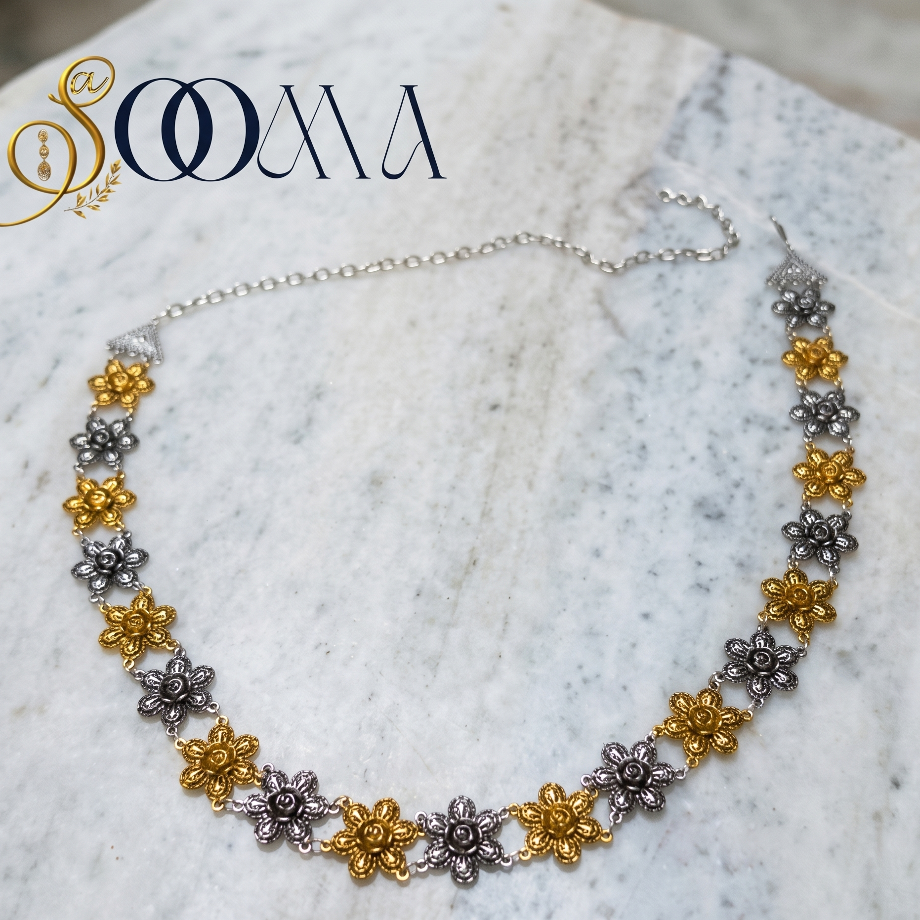 Waistband with floral designs in gold and silver on a marble surface, featuring the brand 'Sooma'.