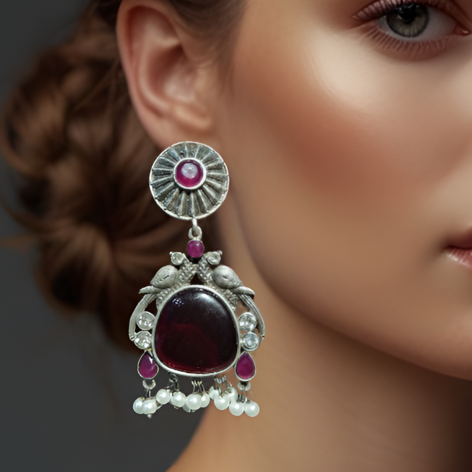 Close-up of a woman wearing an ornate earring with a dark gemstone and pink stones.